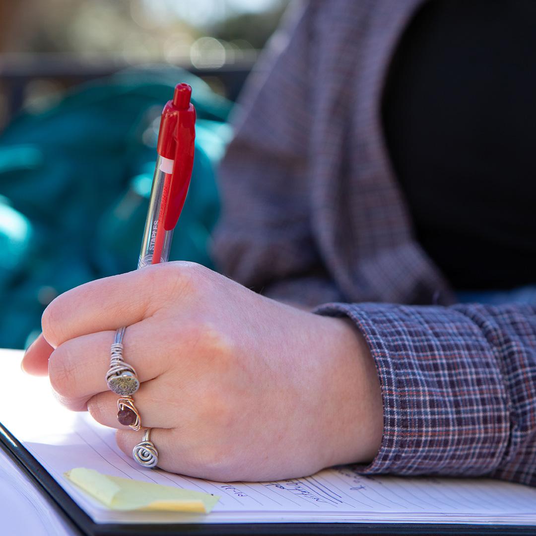 Student taking notes with a red pen